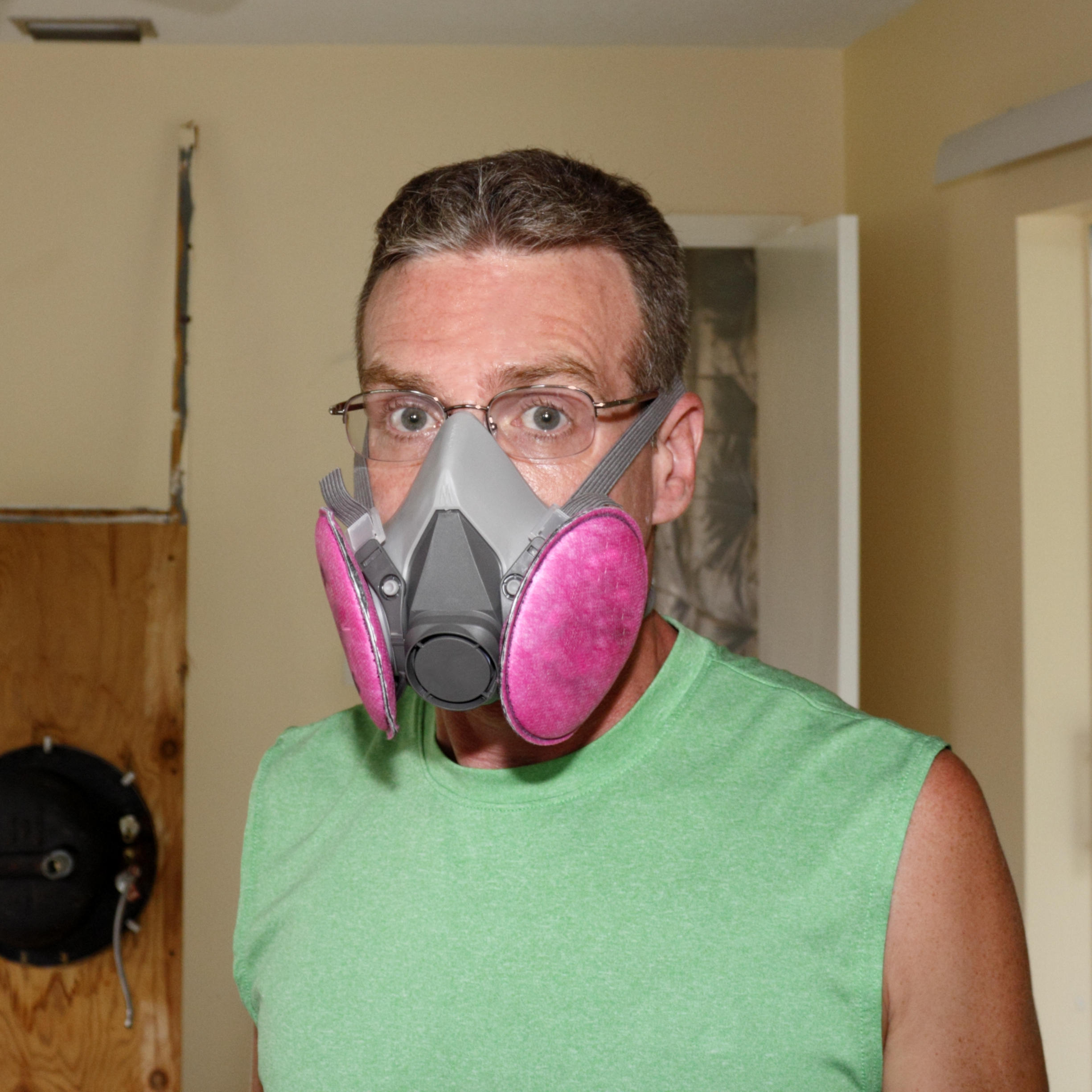 Caucasian man wearing a pink and gray ventilator mask that helps protect his health from mold as he works on a home renovation project.